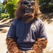 A person in a lion mask wearing a dark gray Hoonigan TOPOGRAHPHIC TERRAIN short sleeve tee outdoors on a sunny day.