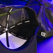 Close-up of a black Hoonigan HITS V2 trucker hat showing interior mesh lining, branded tape, and a partial view of the hat's structured crown.