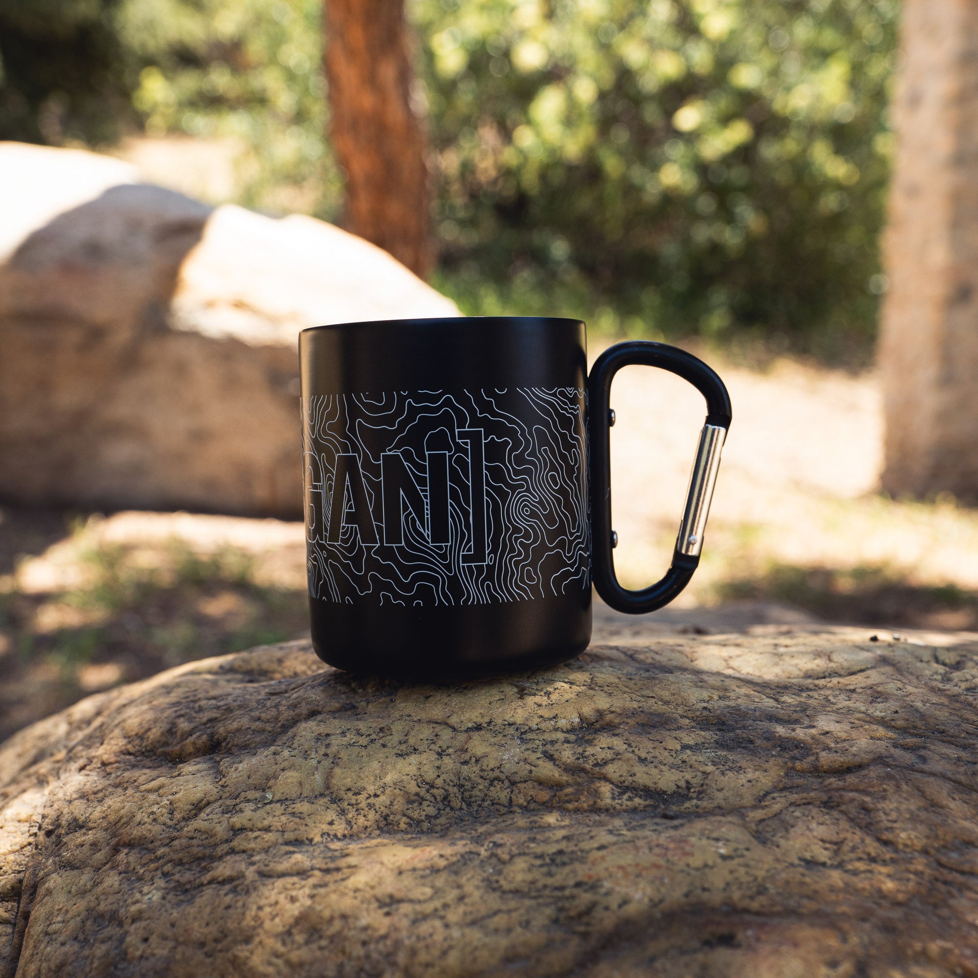Black mug with topographic map design and carabiner handle, ideal for outdoor adventures and camping.