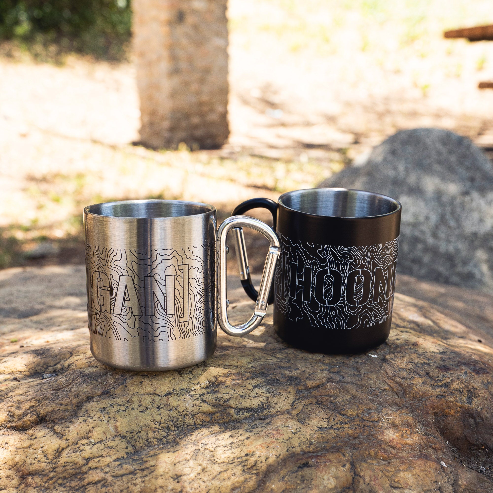 Hoonigan TOPOGRAPHIC CENSBOR BAR Carabiner Mug set with engraved topographic design, placed on a rock outdoors.