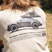 Back of a beige T-shirt featuring a graphic of a vintage car with a rooftop tent, and text about the Hoonigan Adventure Vehicle Overland Collective.