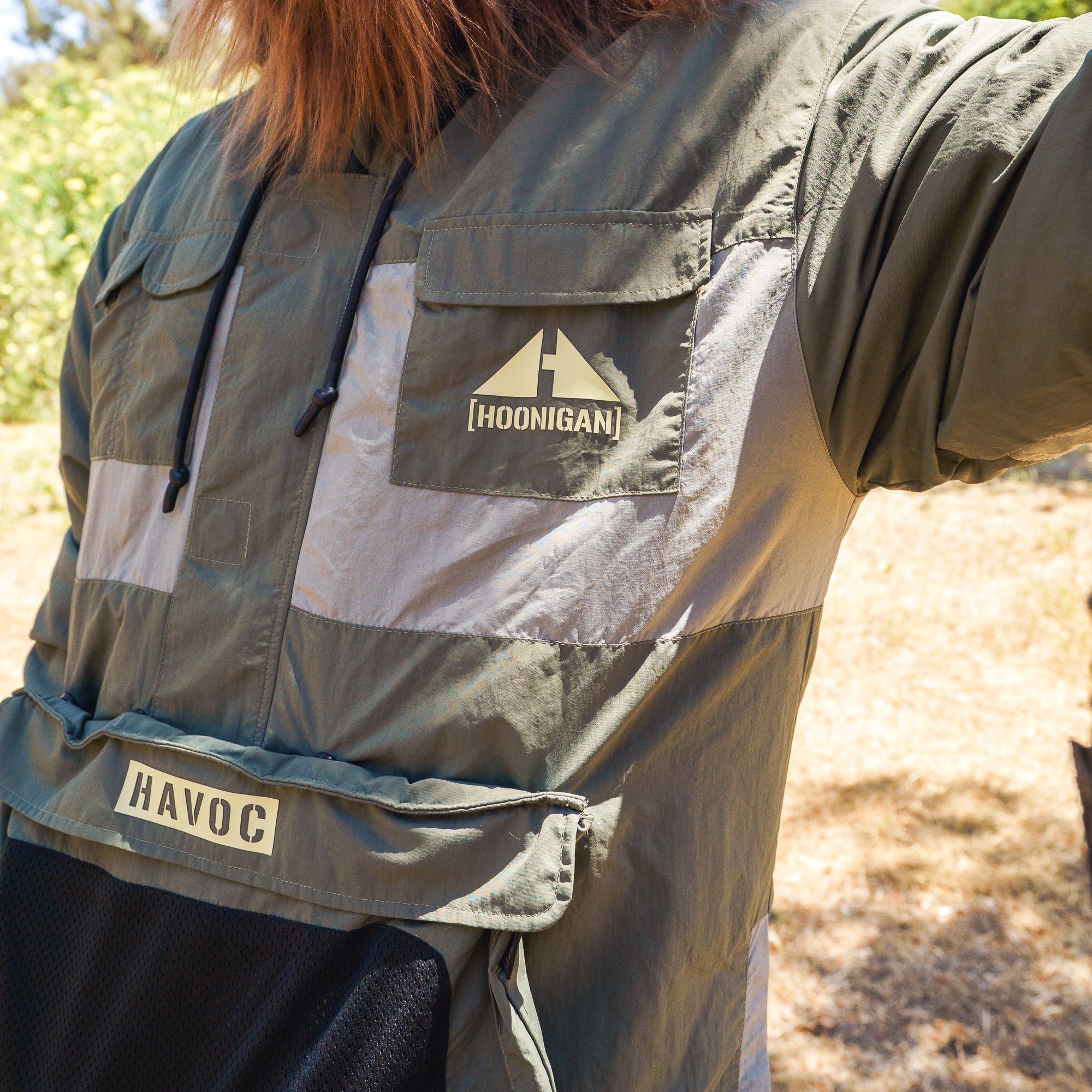 Close-up of a Hoonigan H.A.V.O.C. rain-activated windbreaker jacket with logo patches, worn outdoors in sunlight.