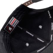 Close-up of the inside of a black snapback hat featuring "Hoonigan" branding on the inner band and a "BRACKET X LOGO" patch on the brim.
