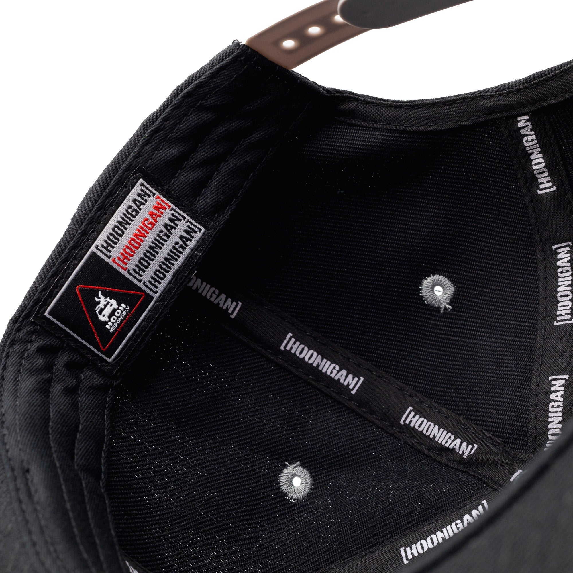 Close-up of the inside of a black snapback hat featuring "Hoonigan" branding on the inner band and a "BRACKET X LOGO" patch on the brim.