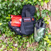 Hoonigan OH SH*T Safety Kit with first aid supplies and a firearm holster, placed on green ivy and tree bark.