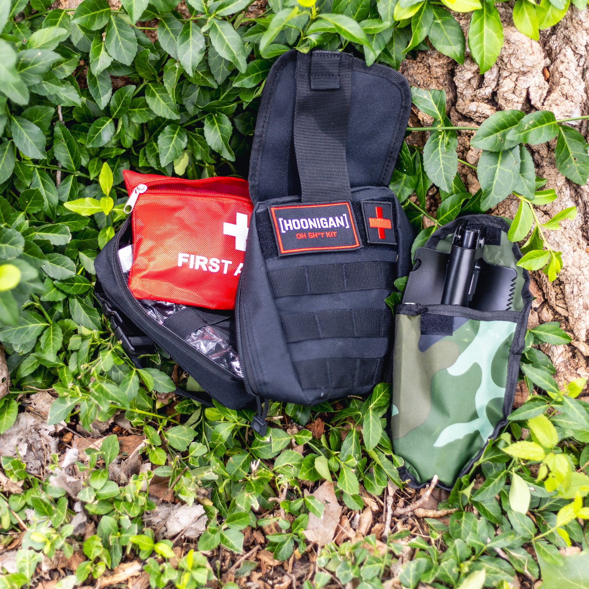 Hoonigan OH SH*T Safety Kit with first aid supplies and a firearm holster, placed on green ivy and tree bark.