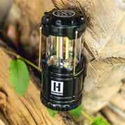Hoonigan H.A.V.O.C. lantern mounted on a wooden surface outdoors, featuring a black body, clear protective glass, and the Hoonigan logo.
