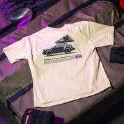 Cream-colored T-shirt with a graphic of a vintage car with a tent on top, featuring "Hoonigan Adventure Vehicle Overland" text.