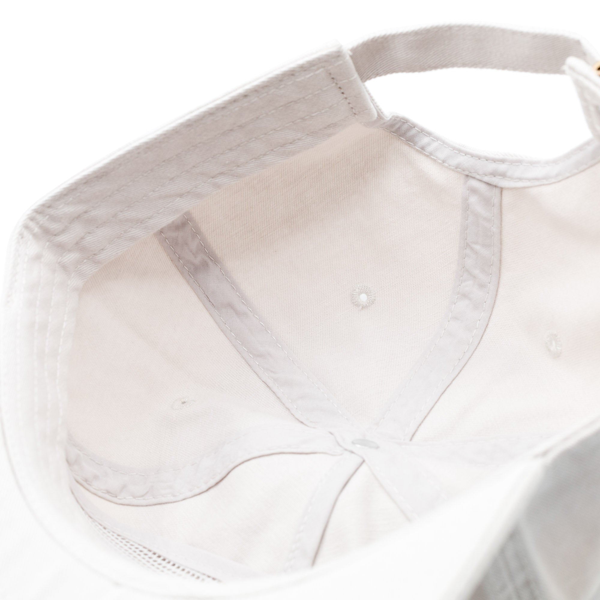 Close-up of the inside of a white unstructured strapback hat with visible stitching and ventilation eyelets.