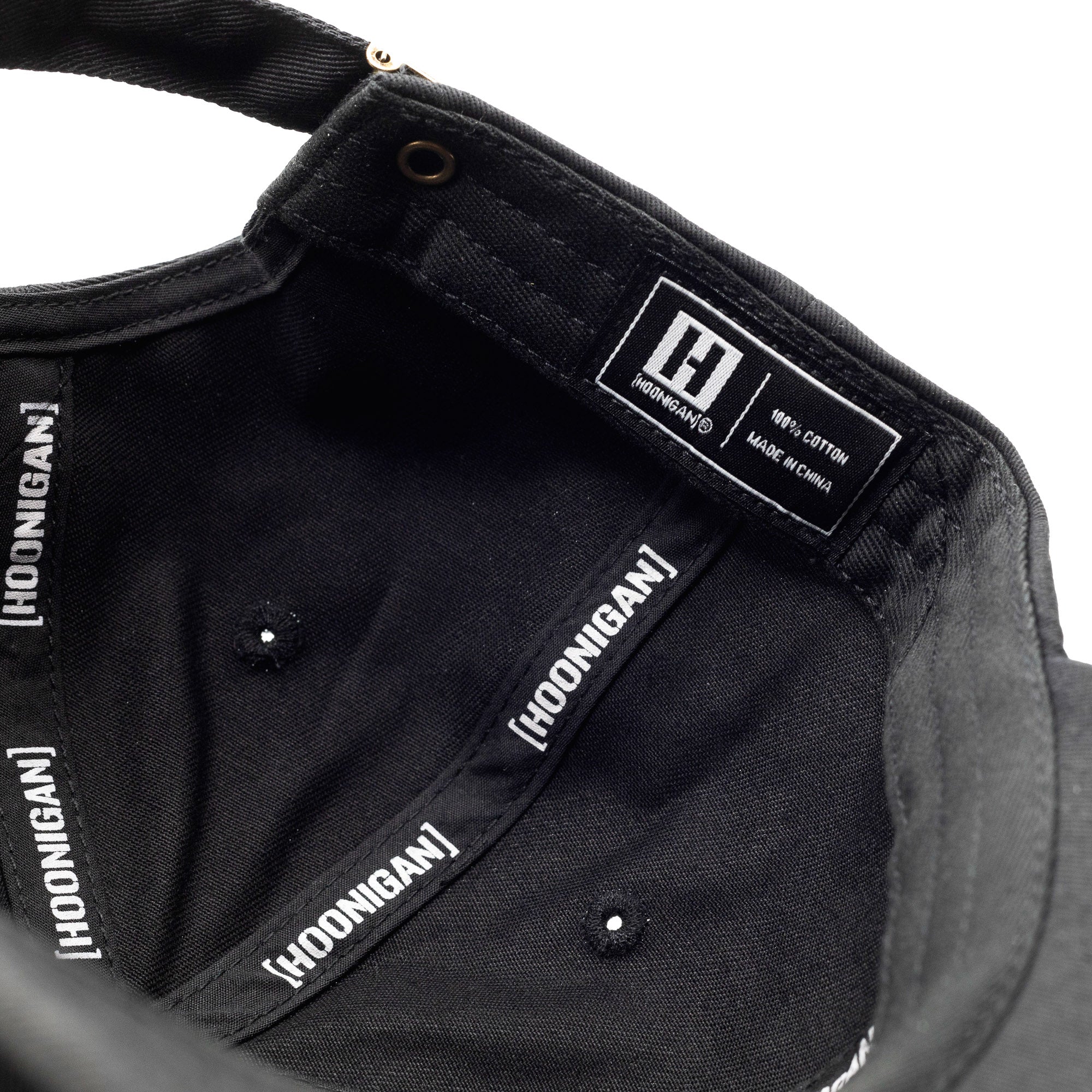 Close-up of the inside of a black unstructured strapback hat featuring white "Hoodgang" branding on the inner band and label, made of 100% cotton.