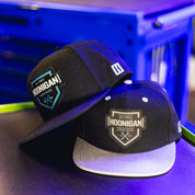 Two black snapback hats with "Hoonigan Industries" patches, one with a gray brim, displayed on a dark surface.