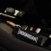 Hoonigan x Sayaka LIFE IS A CHALLENGE Jet Tag Keychain in black and pink, featuring bold text and a sturdy metal keyring.