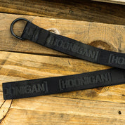 Hoonigan CAUTION TAPE Reversible Belt displayed on wooden surface, featuring a bold black design and durable buckle.