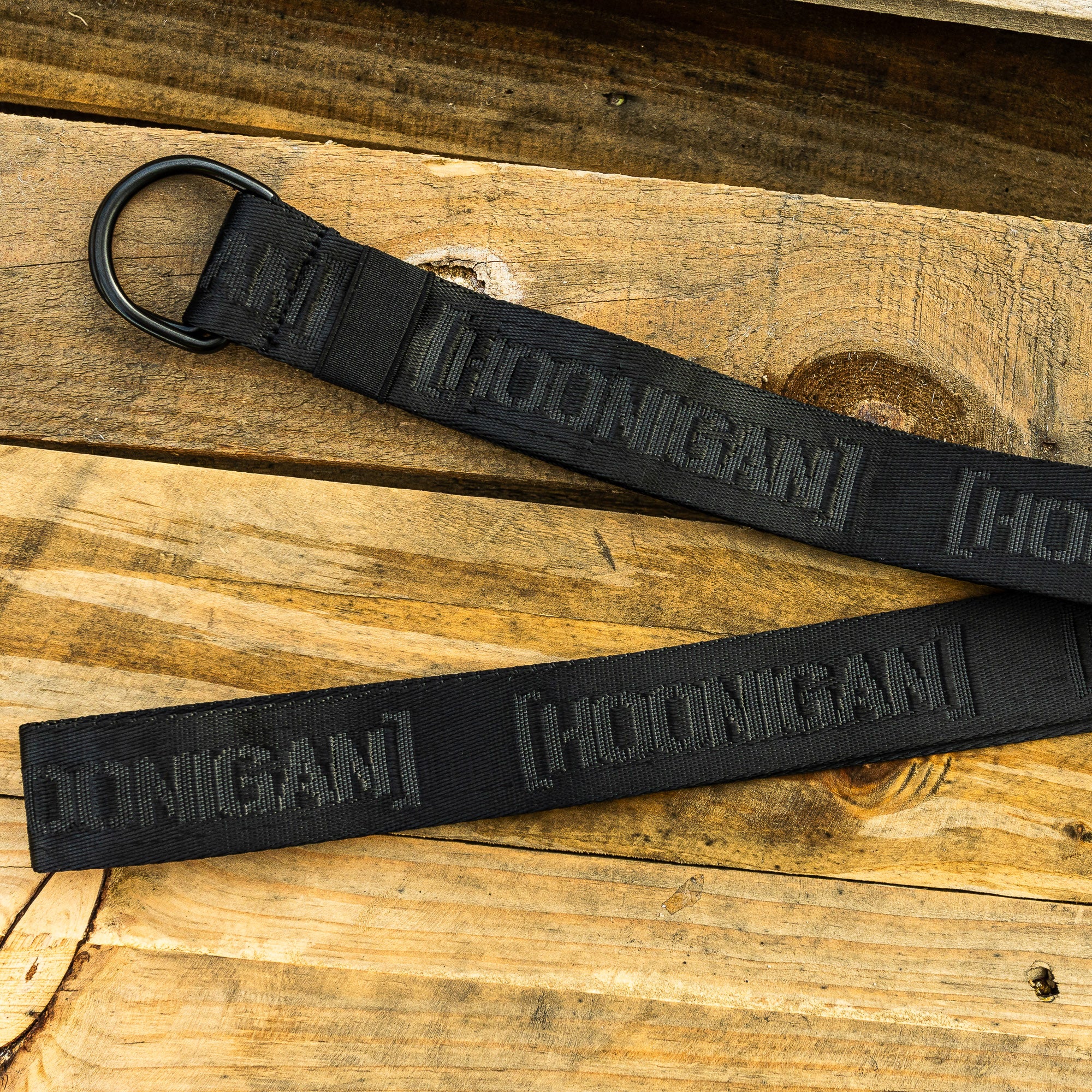 Hoonigan CAUTION TAPE Reversible Belt displayed on wooden surface, featuring a bold black design and durable buckle.