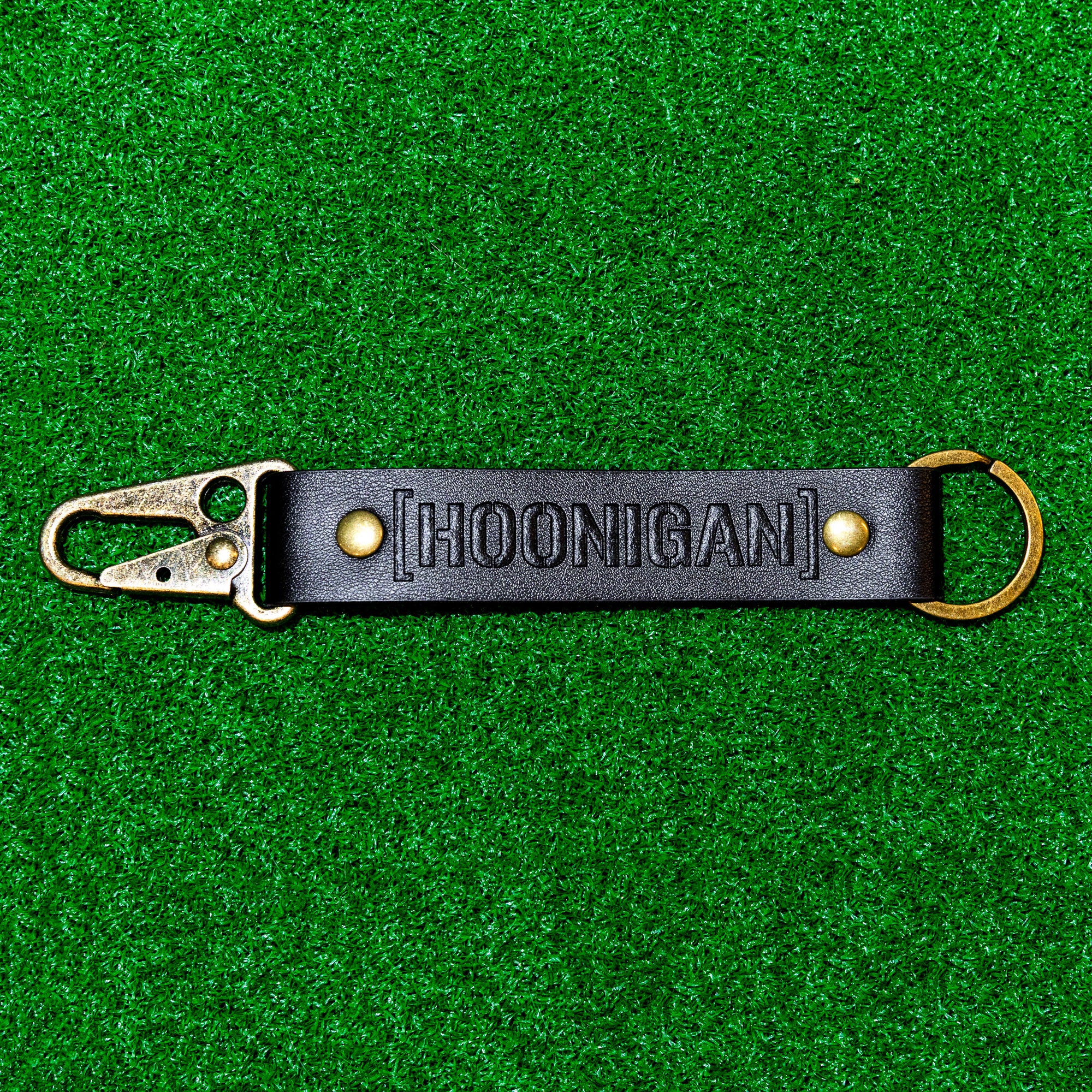 Hoonigan leather keychain featuring a bold logo and a sturdy clip, perfect for automotive enthusiasts.