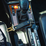 Hoonigan leather keychain featuring a bold logo, resting on a car's center console with keys and cassette tapes.