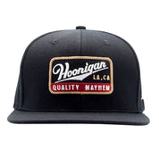 Black snapback hat featuring a Hoonigan logo patch with "Quality Mayhem" text, perfect for motorsport enthusiasts.