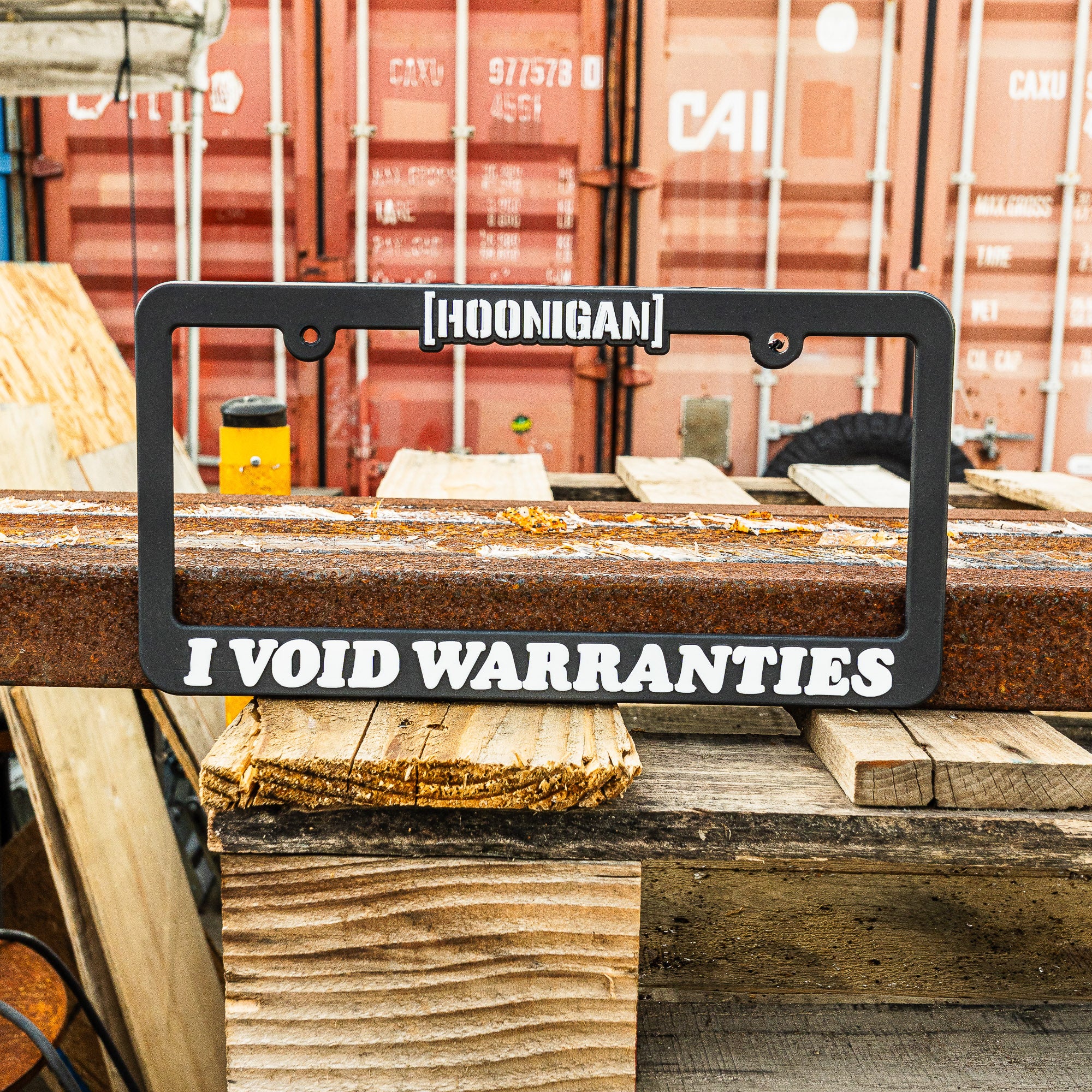 Hoonigan VOID license plate frame featuring bold text that reads "I VOID WARRANTIES" on a rugged background.