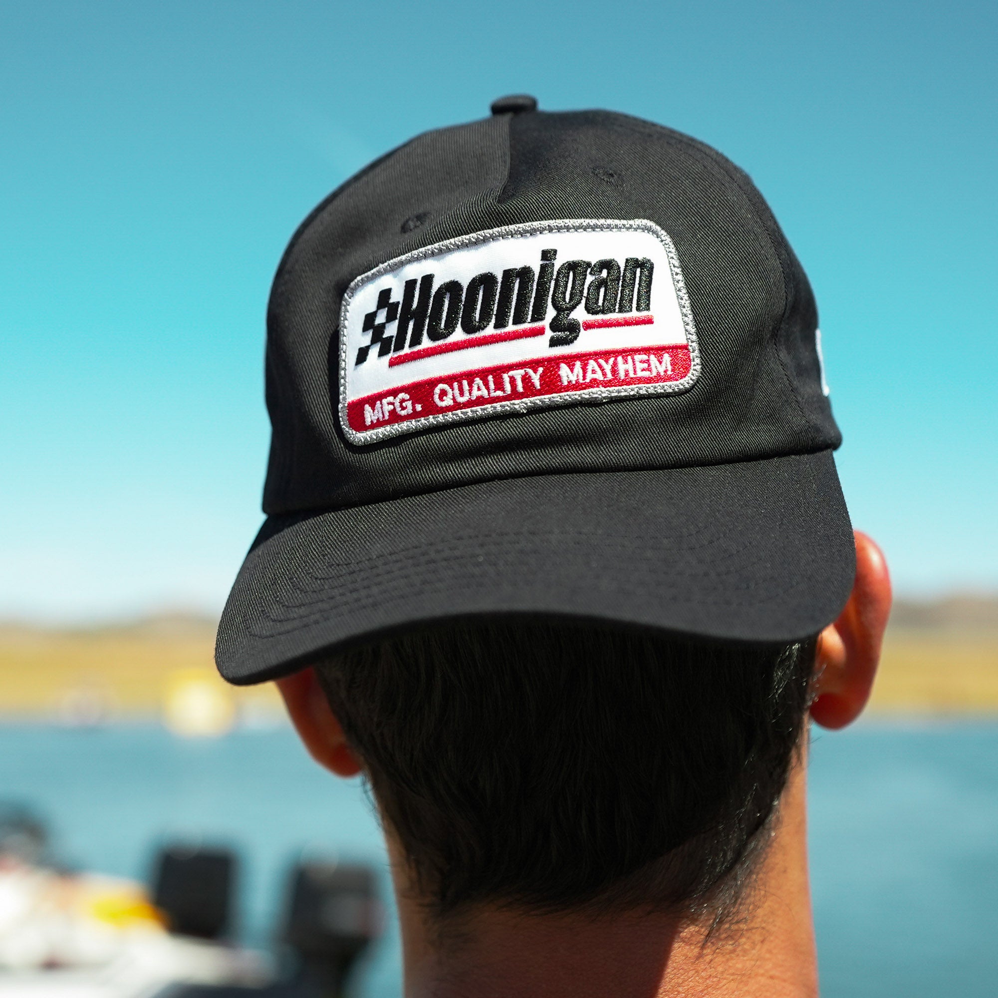 Black unstructured strapback hat featuring Hoonigan logo and "MFG. QUALITY MAYHEM" patch, perfect for motorsport enthusiasts.