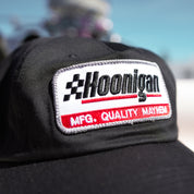 Black unstructured strapback hat featuring a Hoonigan logo patch with "MFG. QUALITY MAYHEM" text, ideal for motorsport fans.