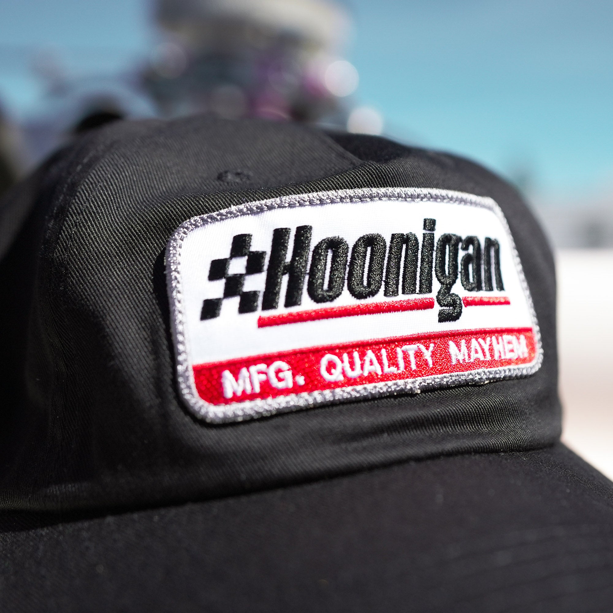 Black unstructured strapback hat featuring a Hoonigan logo patch with "MFG. QUALITY MAYHEM" text, ideal for motorsport fans.
