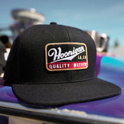 Hoonigan Champagne Snapback Hat featuring a bold embroidered logo on a black cap, perfect for motorsport enthusiasts.