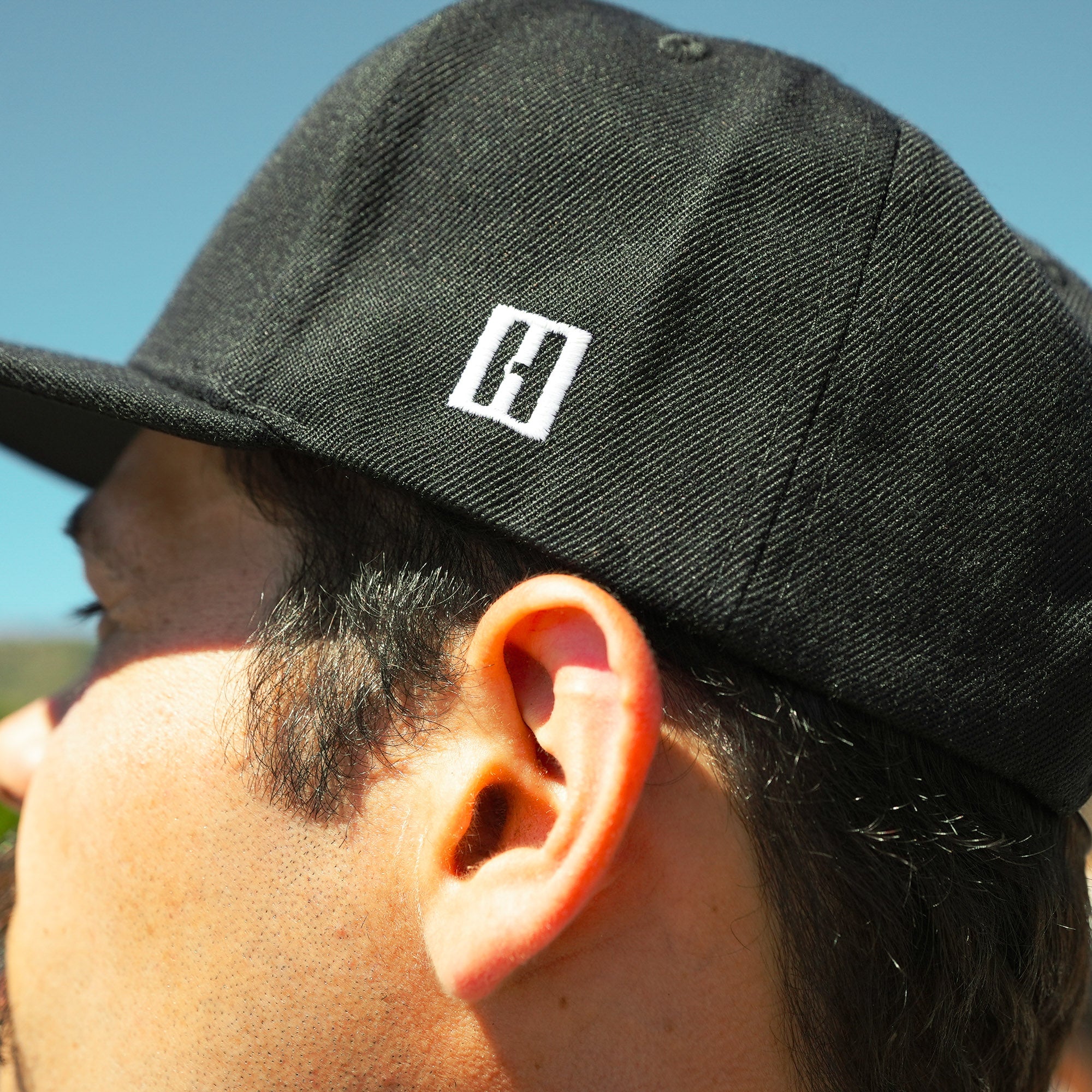 Close-up of a black snapback hat featuring the Hoonigan logo, worn by a person outdoors, showcasing automotive style.