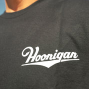 Black short sleeve t-shirt featuring a white Hoonigan logo, ideal for motorsport enthusiasts and car culture fans.