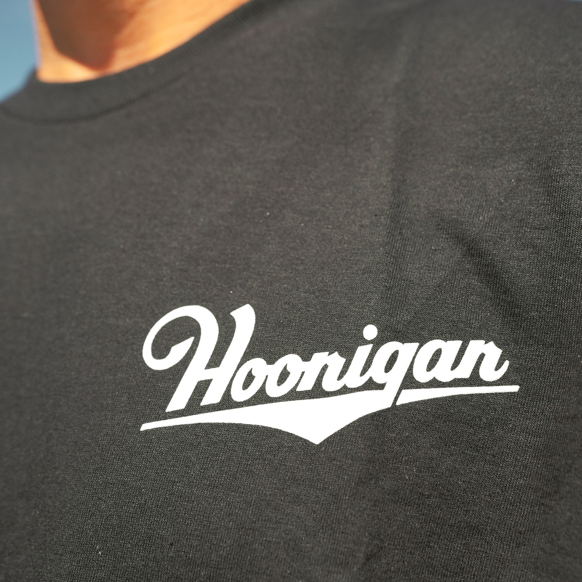 Black short sleeve t-shirt featuring a white Hoonigan logo, ideal for motorsport enthusiasts and car culture fans.