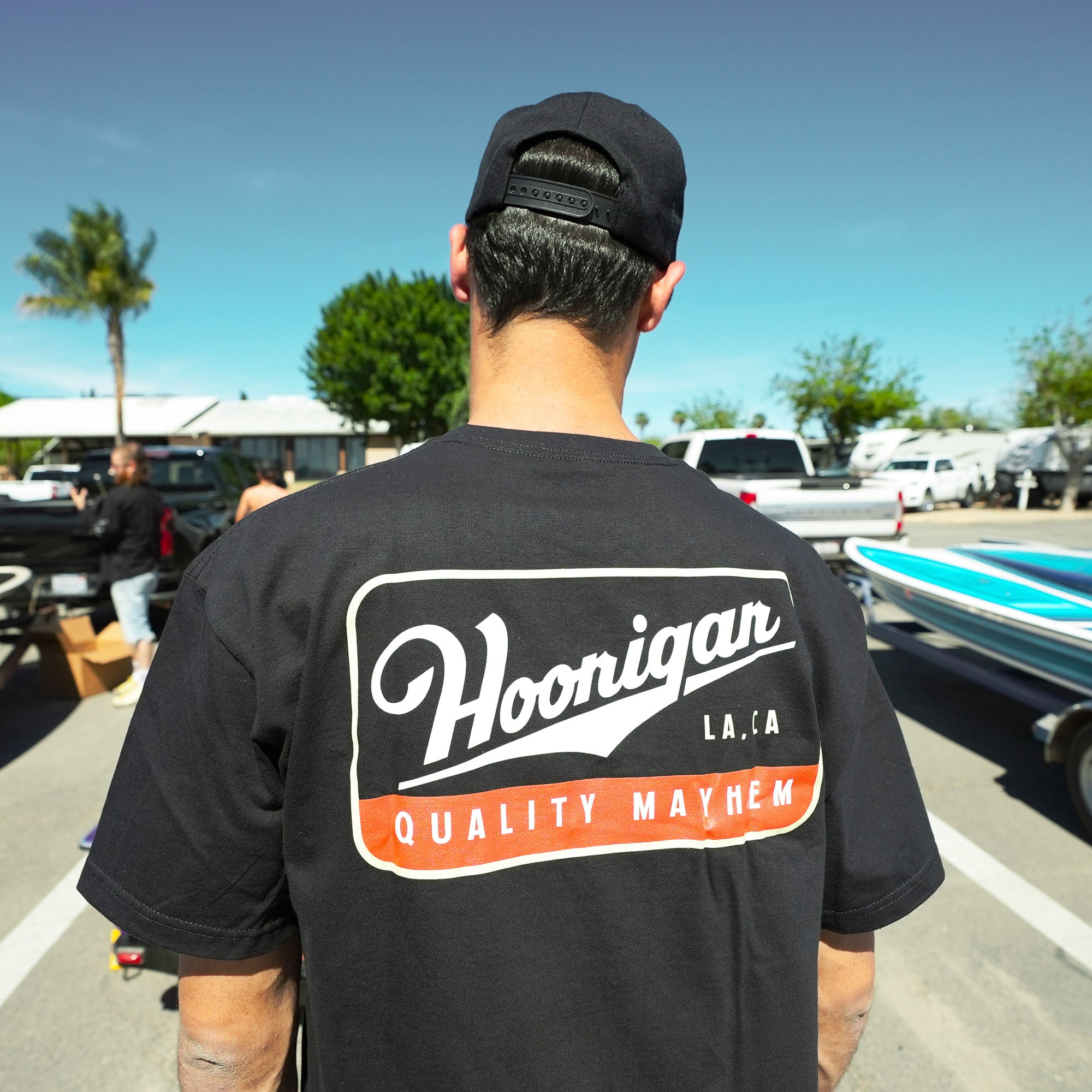 Back view of a man wearing a black Hoonigan CHAMPAGNE short sleeve t-shirt featuring a bold logo and "Quality Mayhem" text.