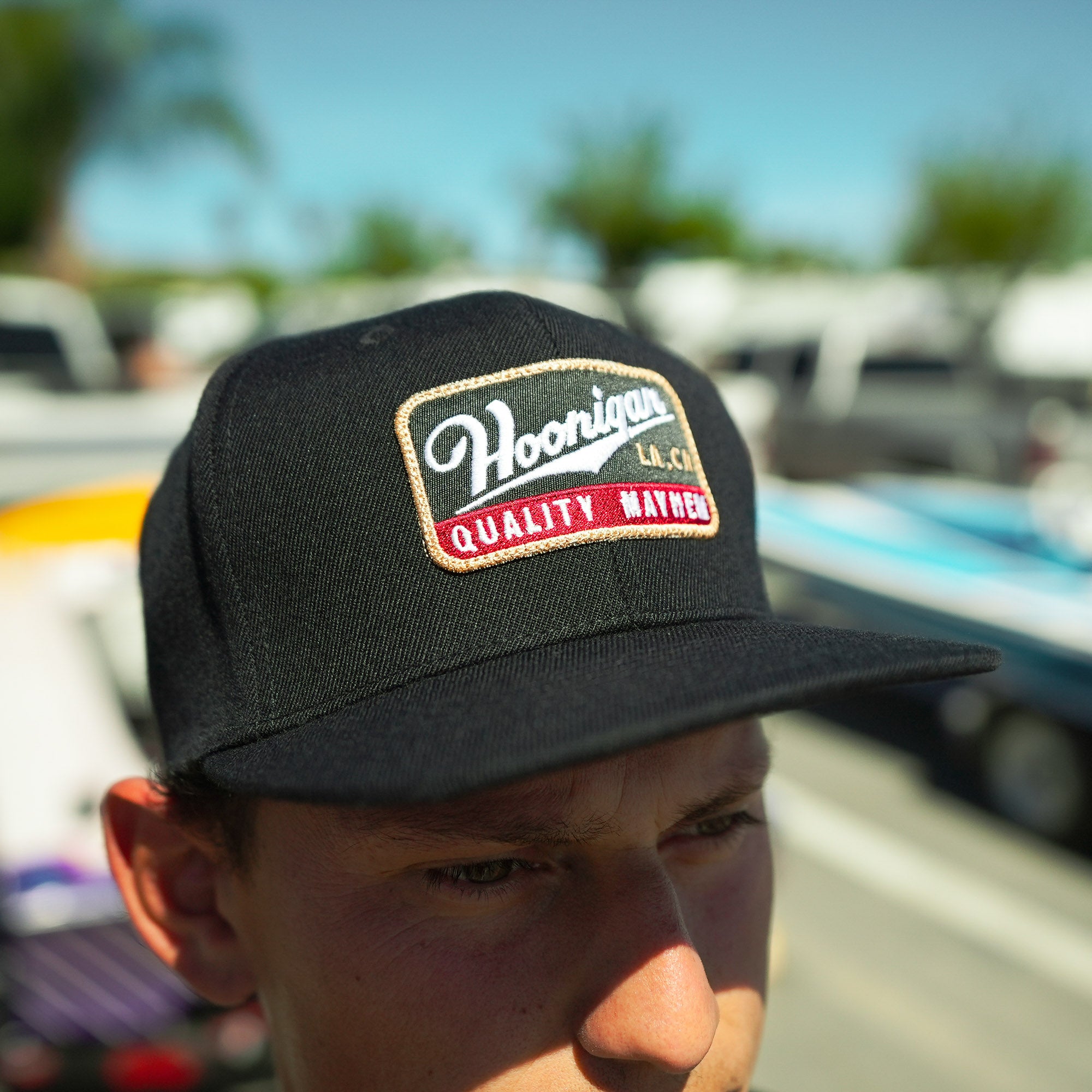 Hoonigan Champagne Snapback Hat featuring a vintage-style embroidered logo on a black cap, perfect for motorsport enthusiasts.