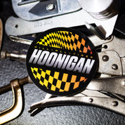 Hoonigan SLIDEWAYS sticker featuring bold lettering and a checkered pattern, placed on a metallic surface with tools.