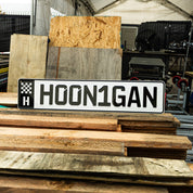 Hoonigan EURO license plate featuring the text HOON1GAN, displayed against a backdrop of wooden planks and workshop materials.