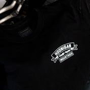 Black Hoonigan CRANKED short sleeve t-shirt featuring a bold white logo on the chest, laid on an engine.