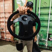 Limited edition Hoonigan steering wheel held by a man, showcasing its sleek design and branding against a colorful backdrop.