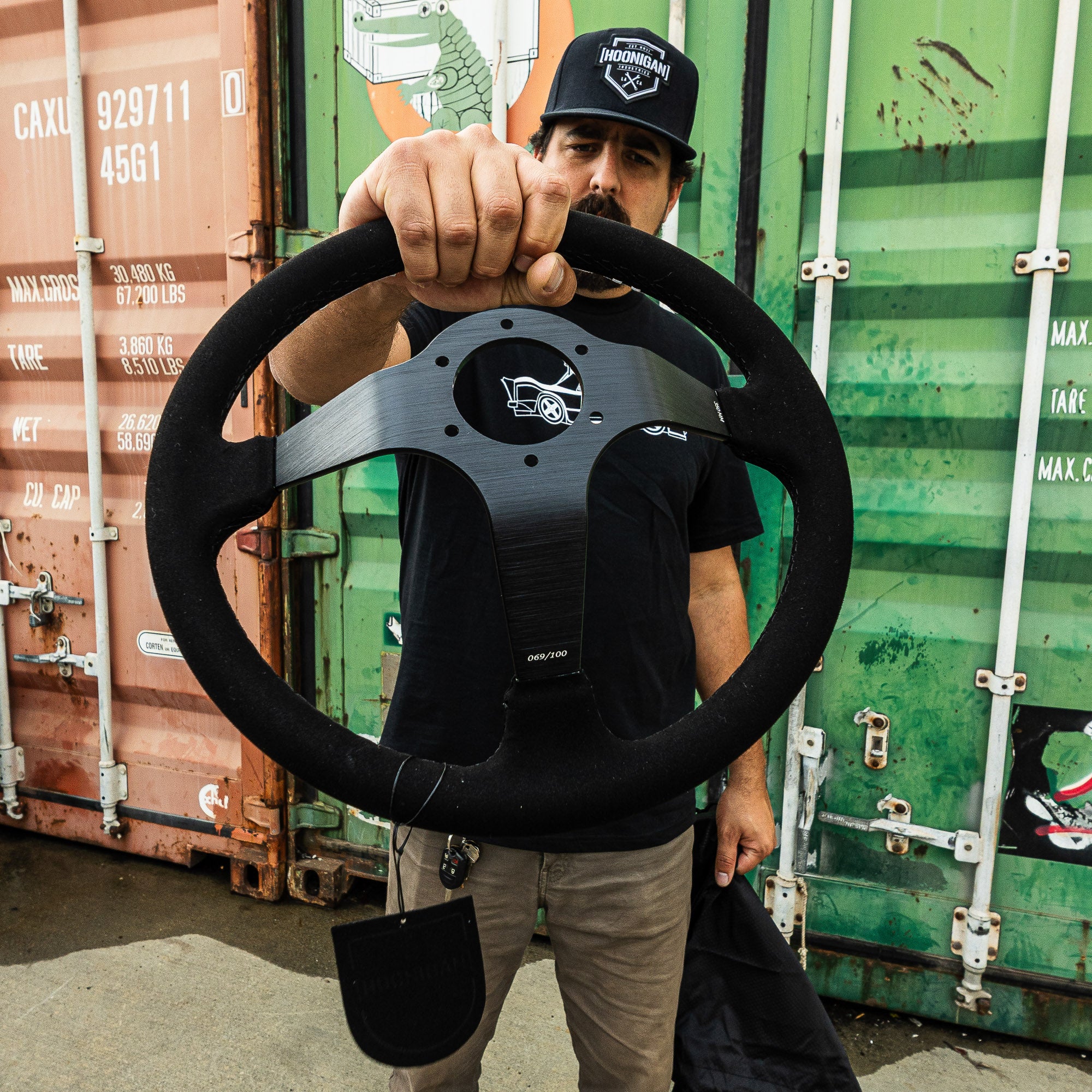 Limited edition Hoonigan steering wheel held by a man, showcasing its sleek design and branding against a colorful backdrop.