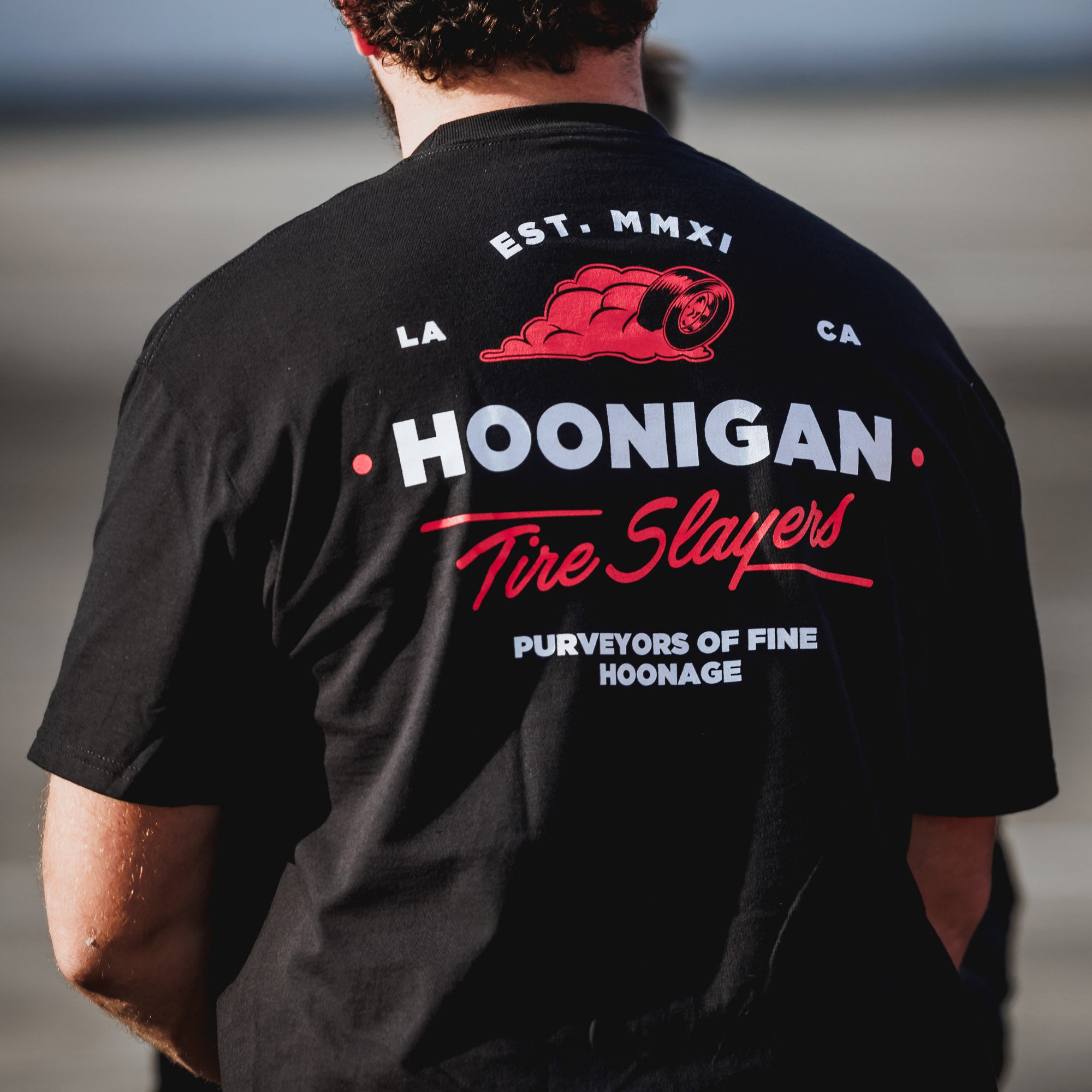 Black short sleeve t-shirt featuring Hoonigan logo and "Tire Slayers" text on the back, perfect for motorsport enthusiasts.