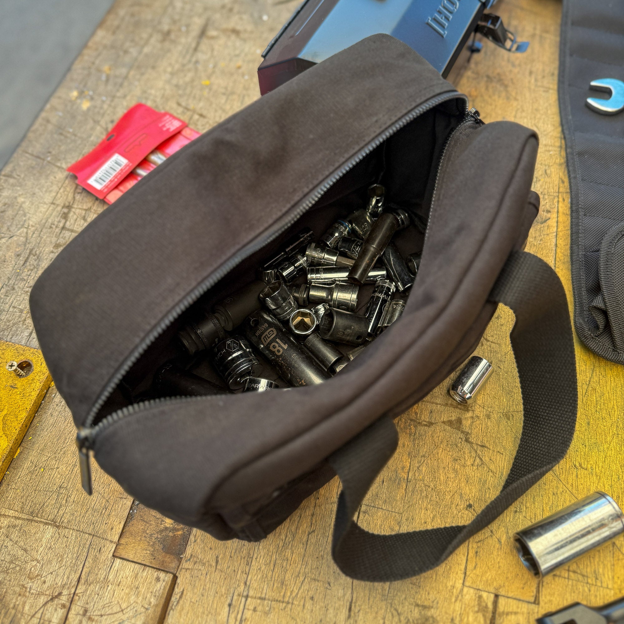 Hoonigan CENSOR BAR Tool Bag filled with various metal sockets and tools, resting on a wooden workbench.