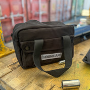 Hoonigan CENSOR BAR Tool Bag in black, featuring a sturdy handle and front pocket, placed on a wooden workbench.