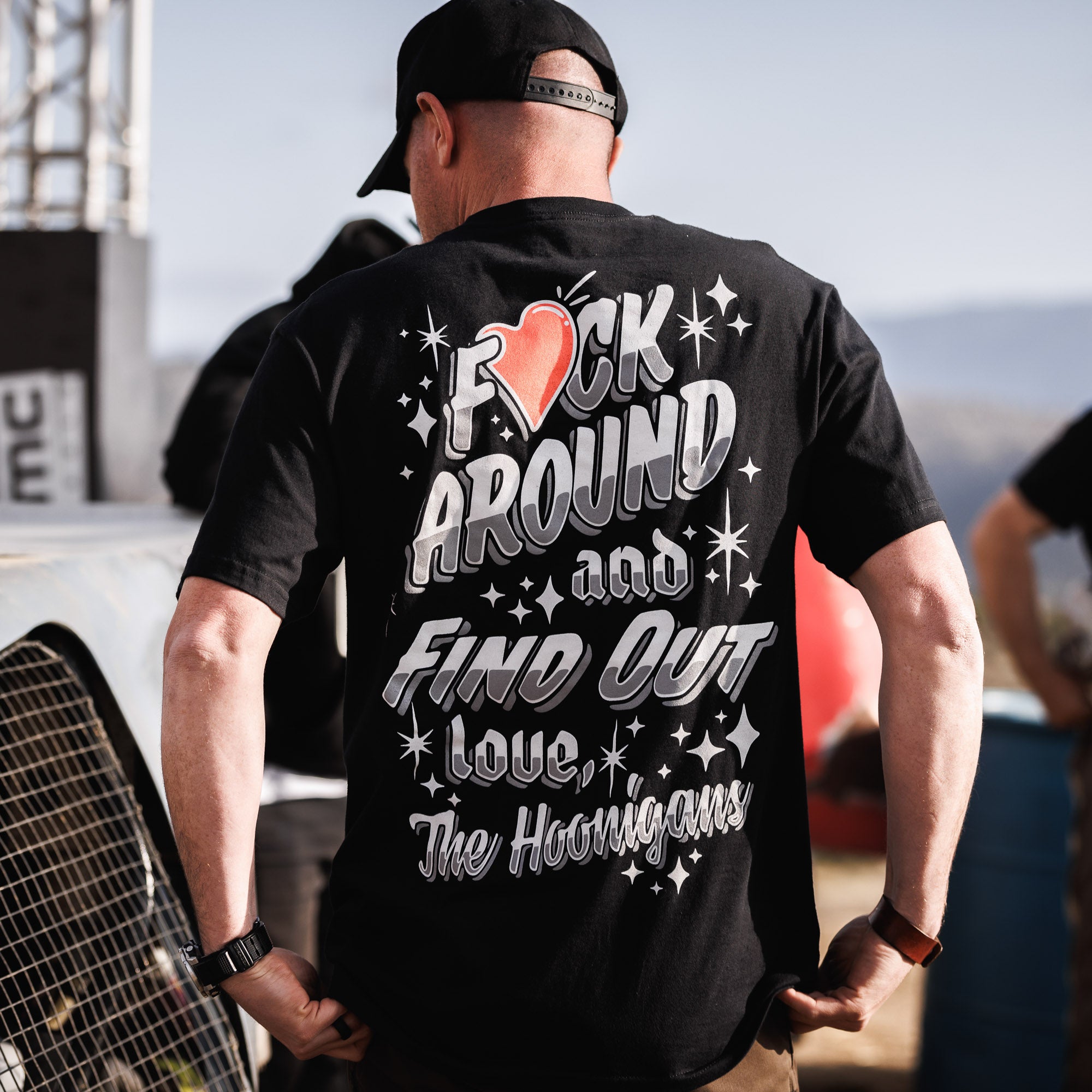 Back of black Hoonigan FIND OUT V2 short sleeve tee with bold white and gray text, stars, and a red heart graphic.