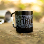 Black ceramic mug with topographic map design and "HOONIGAN" text, featuring a carabiner handle for outdoor use.