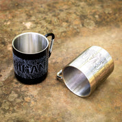 Two metal carabiner mugs with topographic map designs, one black and one silver, on a textured surface.