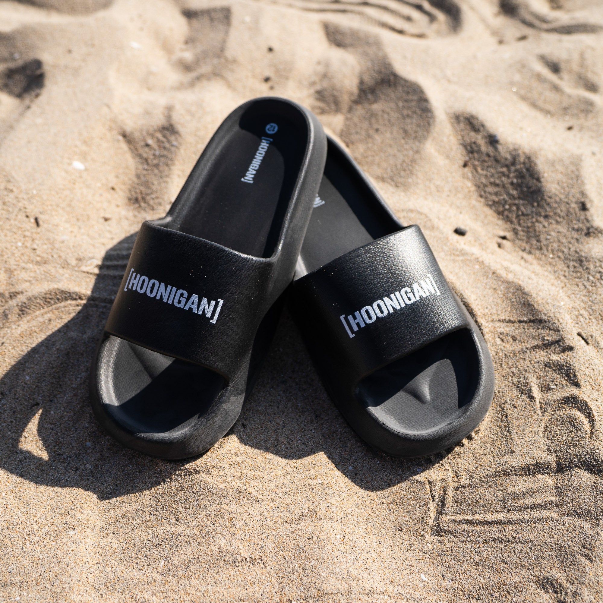 Hoonigan Censor Bar Bracket Logo slides in black resting on sandy beach, showcasing bold logo design.