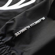 Close-up of a black Rotiform GLOBAL IMPACT half-zip anorak jacket with white coordinates printed on the fabric.