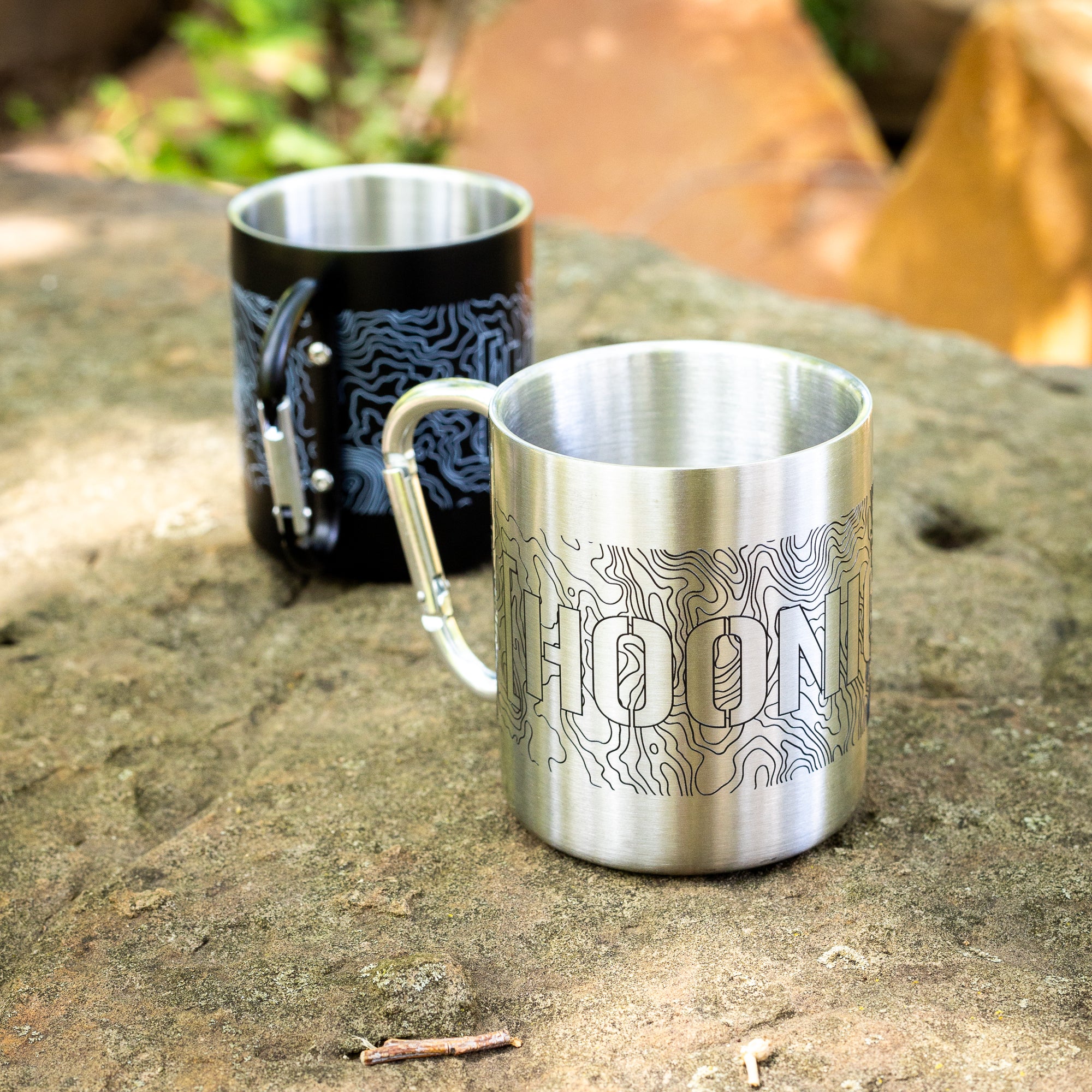 Stainless steel mug with topographic map design and attached carabiner, ideal for outdoor adventures and camping.