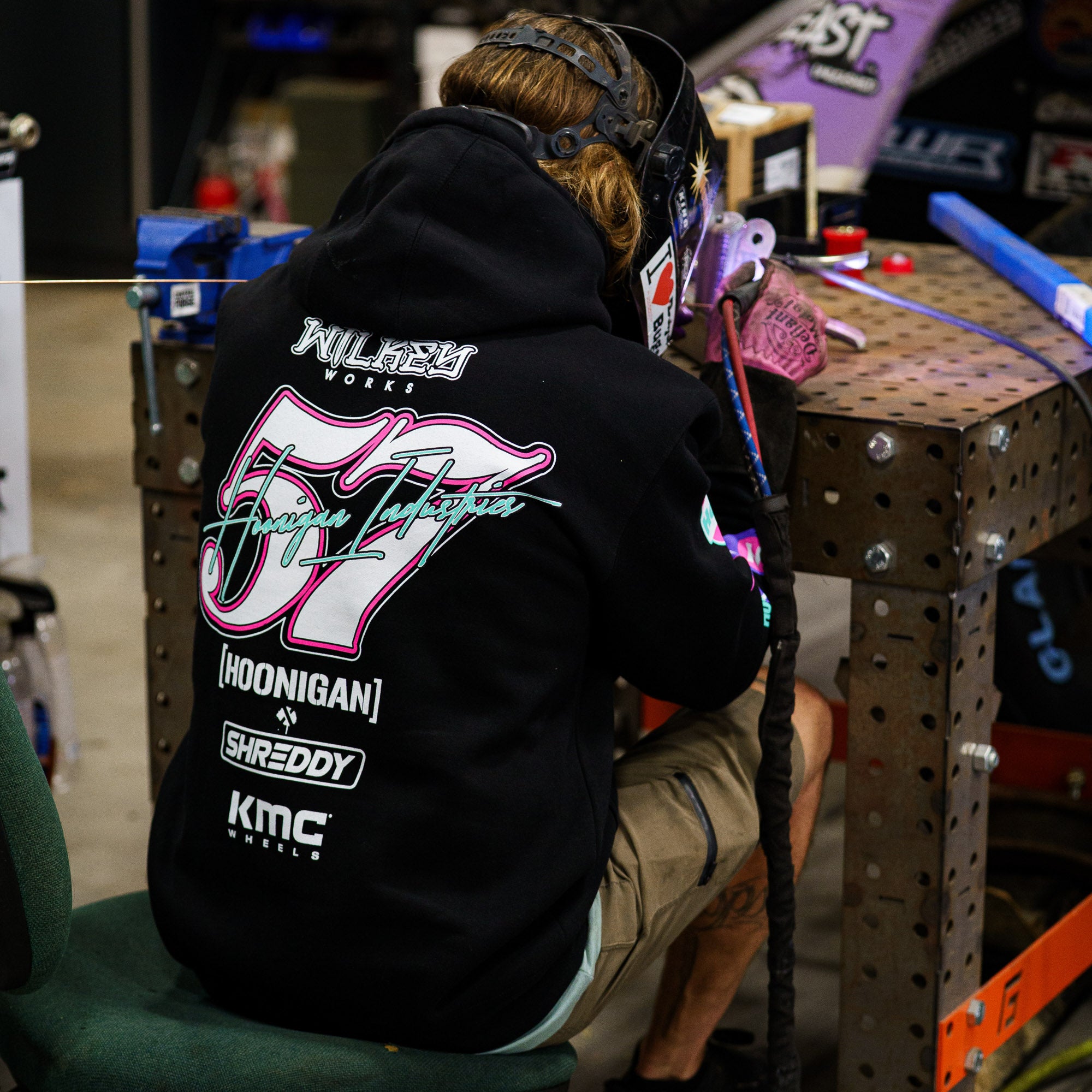 Hoonigan x Shreddy pullover hoodie featuring vibrant graphics, worn by a person welding in a workshop setting.