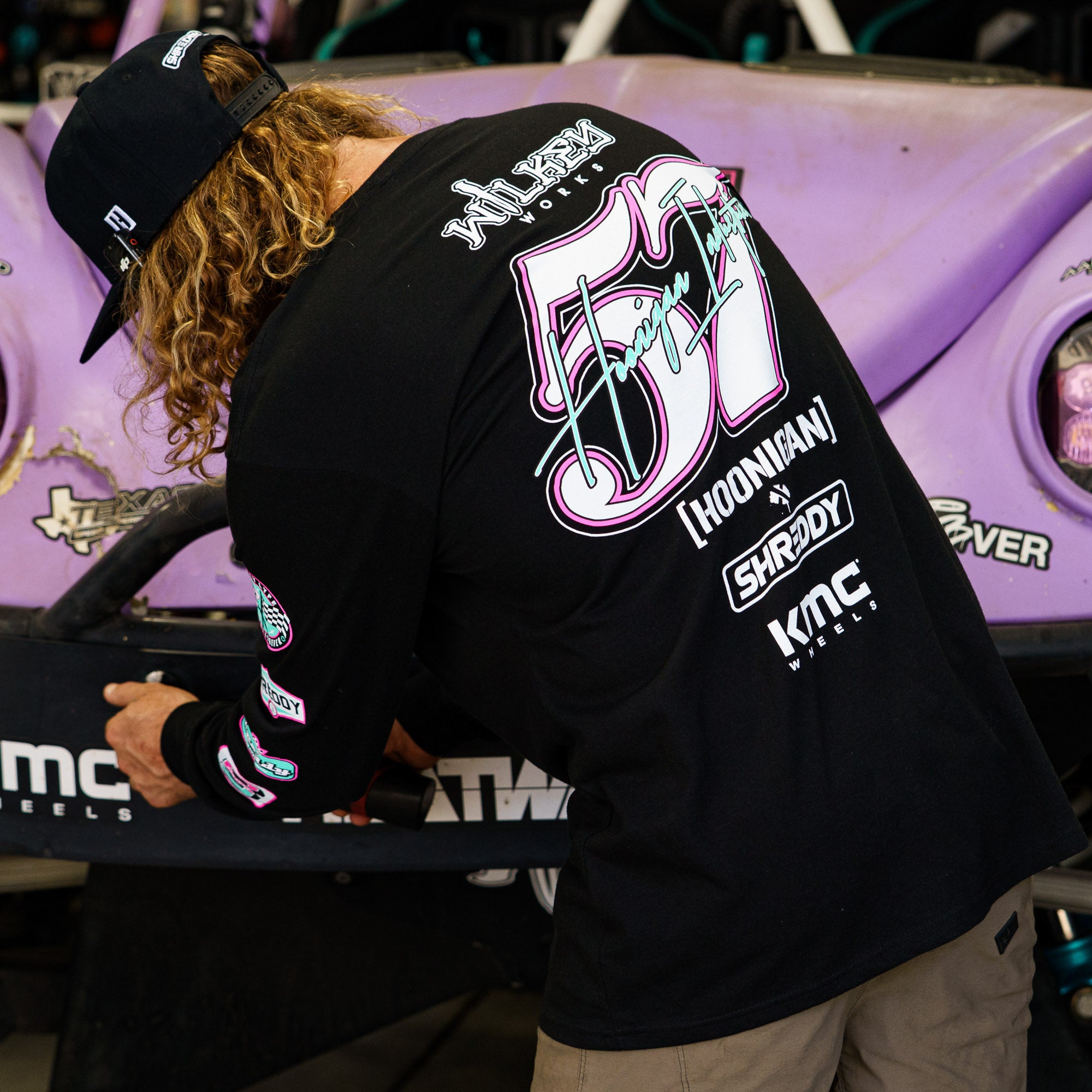 Hoonigan x Shreddy 57 long sleeve t-shirt worn by a mechanic working on a purple race car in a garage setting.