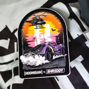 Hoonigan x Shreddy DESERT Sticker featuring a vibrant off-road vehicle and helicopter against a sunset backdrop.