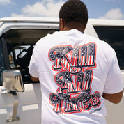 Back view of a man wearing a white T-shirt with bold red, black, and white graphic text and design, standing near a vehicle.