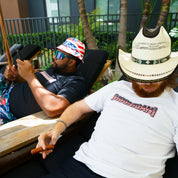 Two men relaxing outdoors, wearing Hoonigan branded short sleeve T-shirts and stylish hats, one with a patriotic American flag hat.